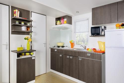 La cuisine est équipée de placards bruns et d'un réfrigérateur blanc. dans l'établissement Les Acacias, à Vercheny