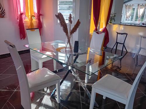a glass dining room table with white chairs and a vase at La ROSE ISLAND in Grand-Bourg
