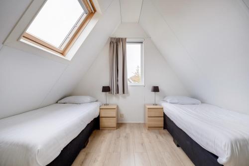 two beds in a attic bedroom with two windows at Gele Kwikstaart I Ruime Woning met Omliggende Tuin in Zwiggelte
