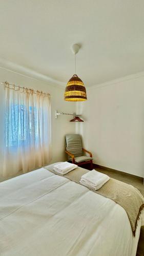 a bedroom with a large white bed and a chair at Vela de Estai in Vila Nova de Milfontes