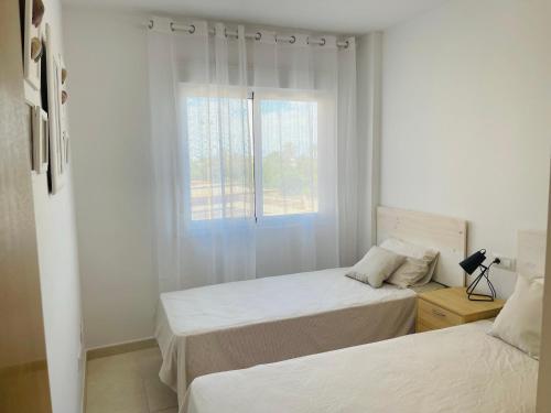two beds in a white room with a window at Jardines de Veneciola by Alina365 in La Manga del Mar Menor