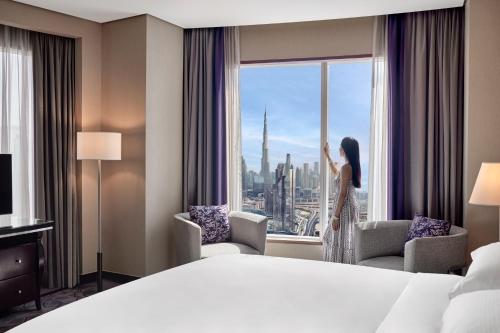 a woman standing in a hotel room looking out the window at Rose Rayhaan by Rotana - Dubai in Dubai