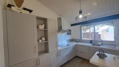 une cuisine avec des armoires blanches, un évier et une fenêtre dans l'établissement LES MUGUETS - Maison 4 chambres à 600m de la plage, à Saint-Hilaire-de-Riez