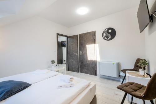 a white bedroom with a bed and a chair at JIN JANG Apartman Veszprém in Veszprém