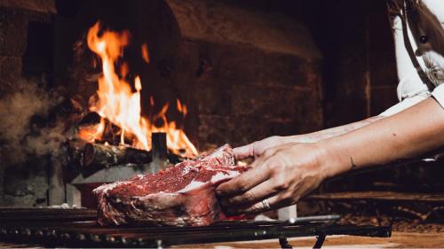 a person holding a piece of meat in front of a fire at Albergo Giovanni Da Verrazzano in Greve in Chianti