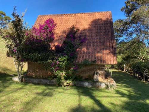 a brick house with a red roof with purple flowers at Pousada Sotaque Mineiro in Cunha