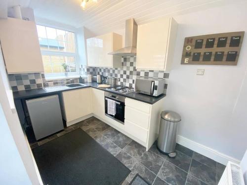 una cucina con armadietti bianchi e ripiani neri di 43 Heol Maelor- A Homely Cottage in Wrexham, North Wales a Coedpoeth
