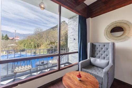 a room with a large window with a chair and a table at Echor Himalayan Aurum Manali, Heating & Cooling in Manāli