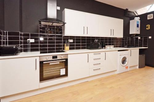 a kitchen with white cabinets and a black tile wall at Townhouse PLUS @ 301 West Street Crewe in Crewe