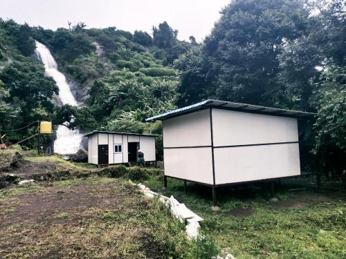 two white buildings on a hill with a waterfall at Campia Homestay Kookal in Kodaikānāl