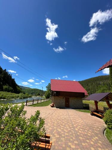 a building with a red roof and benches next to a river at Садиба "Джерело" in Yaremche