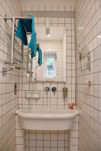 La salle de bains est pourvue de carrelage blanc, d'un lavabo et d'un miroir. dans l'établissement Villa Antoinette, à Saint-Nectaire