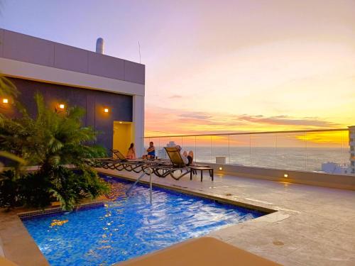 a pool on the roof of a building with people sitting at Exclusivos apartasuites Ambar Roca - Rodadero in Santa Marta