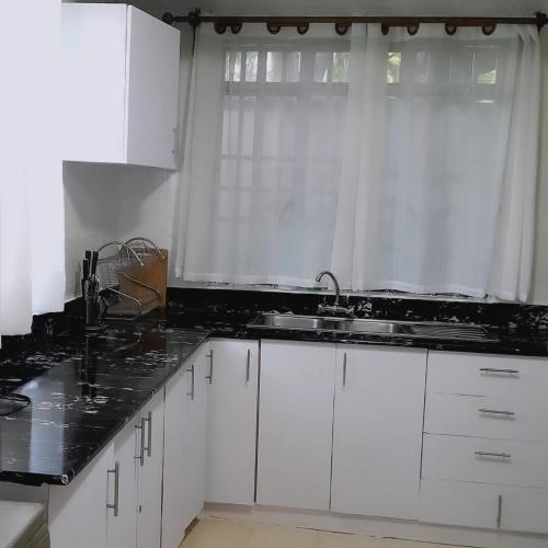 a kitchen with white cabinets and a sink and a window at Sofitel Executive 4 bedrooms stand alone Milimani in Kisumu