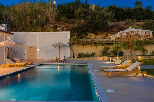 a pool with chairs and umbrellas next to a house at Pantheon Villa Svoronata in Svoronata