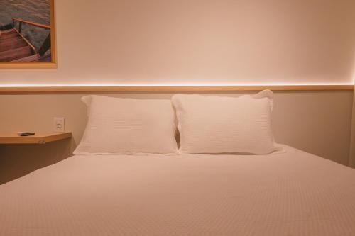 a white bed with two pillows on top of it at Novíssimo com Varanda Gourmet 10 min a pé da praia in Itacimirim