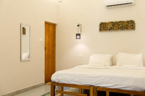 a bedroom with a bed with white sheets and a mirror at Nidra by Sarwaa in Varkala