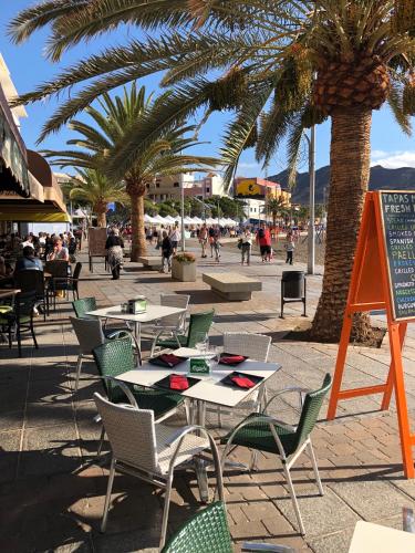 an outdoor cafe with tables and chairs and palm trees at Amazing Sea View apartment with sun drenched terrace! in Gran Tarajal