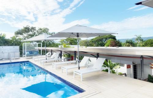 a swimming pool with white chairs and an umbrella at Reef Luxury Apartment in Port Douglas