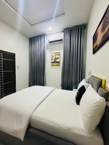 a bedroom with a large white bed and curtains at Hibiscus Empire in Ikota