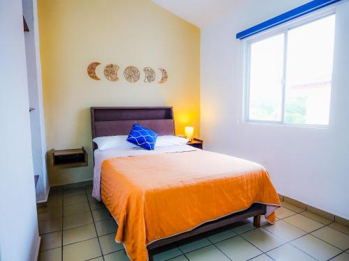 a bedroom with a bed with an orange blanket and a window at Casa Shiloh-depto 3 hab cerca aero y central camionera in Puerto Vallarta