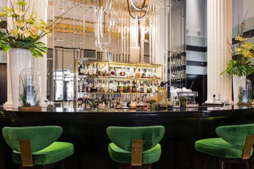 a bar with green chairs in front of a counter at Hotel Bristol, A Luxury Collection Hotel, Warsaw in Warsaw