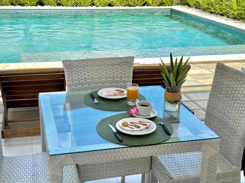 a table with two plates of food on it next to a swimming pool at Caly Pousada in São Miguel do Gostoso