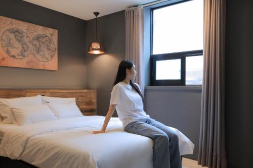 a woman sitting on a bed looking out the window at Hotel Yaja Siheung Jeongwang in Siheung