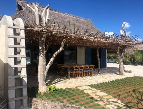 a house with a thatched roof with a table and chairs at Sardine Beach Rote in Pulau Helihana