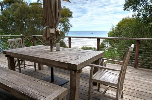 a wooden table and chairs on a deck with an umbrella at Passing Winds - Emu Bay in Emu Bay