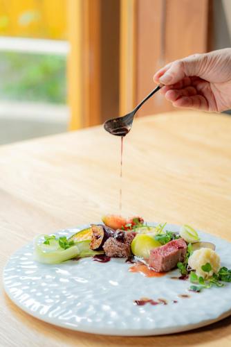 a person holding a spoon over a plate of food at 湯の里いけもり別館 天座 in Himi