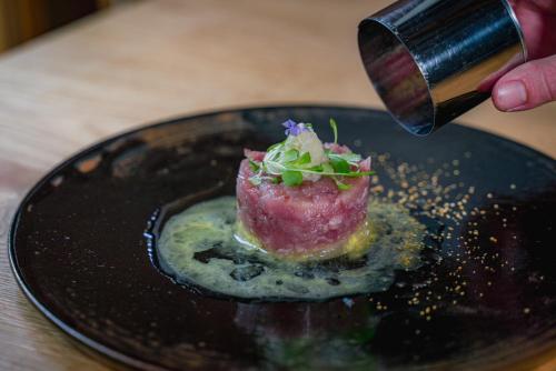 a person is holding a knifeablishangering a dessert on a black plate at 湯の里いけもり別館 天座 in Himi