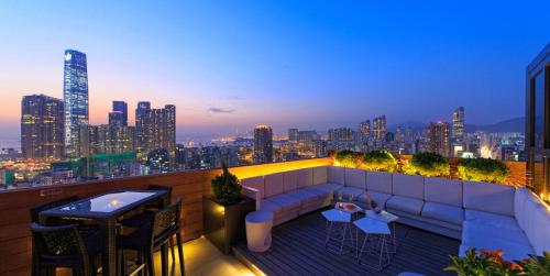 eine Dachterrasse mit einem Sofa, Tischen und einer Skyline der Stadt in der Unterkunft Hotel Madera Hong Kong in Hongkong