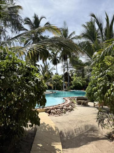 a swimming pool with palm trees in the background at The Nest Tropical Oasis Resort in Paje