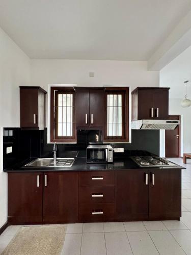 a kitchen with wooden cabinets and a sink and a microwave at Aurora Holiday House in Mount Lavinia