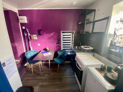 a kitchen with purple walls and a table and chairs at Petite maison au calme avec jardin clôturé les animaux bienvenue in Mollau