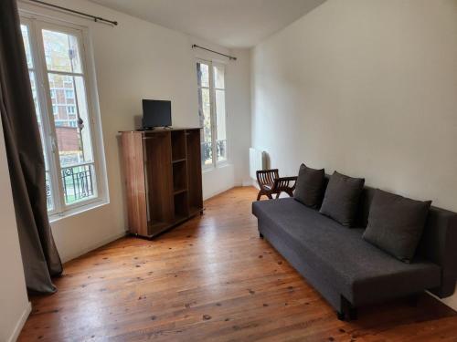 un salon avec un canapé et deux fenêtres dans l'établissement Agréable et vaste Studio à 350 M de Paris, à Gentilly