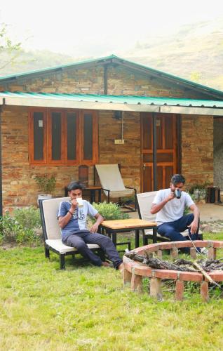two men sitting on chairs in front of a house at Himkosi Farm by the River in Almora