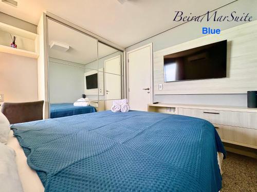 a bedroom with a blue bed and a flat screen tv at Beira Mar Suite in Fortaleza
