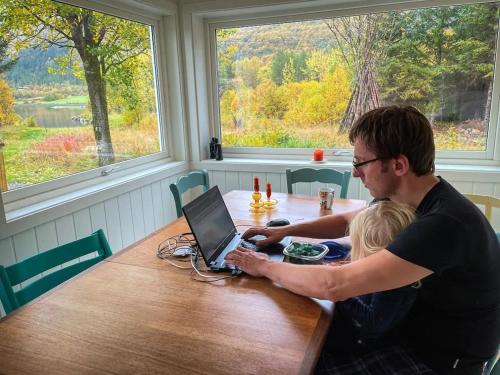 Ein Mann und ein Kind sitzen an einem Tisch mit einem Laptop in der Unterkunft Arctic photo retreat Lofoten - lakehouse Bjørkly in Vestvågøya