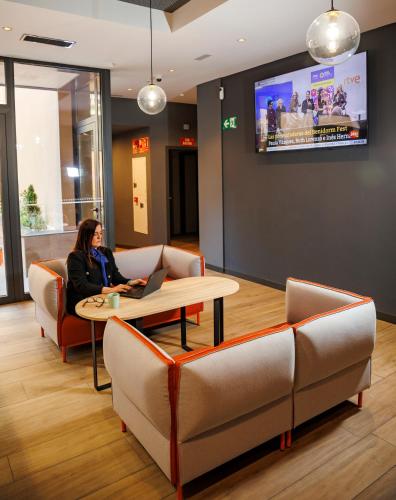 a woman sitting at a table in a waiting room with a laptop at ibis budget Logroño Centro in Logroño