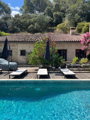 une piscine avec deux parasols et des bancs à côté d'une maison dans l'établissement Villa de pont du Gard, à Remoulins