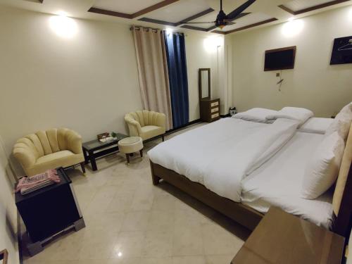 a bedroom with a large white bed and two chairs at AL Fateh Hotel in Lahore