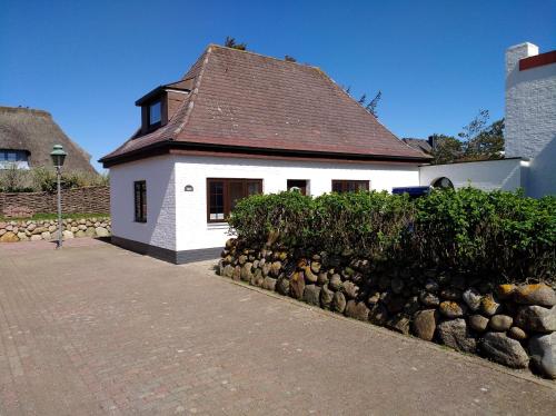 een wit huis met een bruin dak en een stenen muur bij Kiekin in Wenningstedt