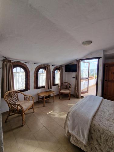 a bedroom with a bed and chairs and windows at Hospedería El Caravansar in Frigiliana