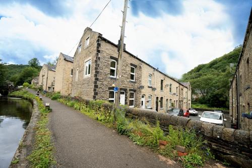 an old brick building next to a canal next to a street at 2BR Modern Hebden Hideaway, Canal side, Stylish and Cosy in Hebden Bridge