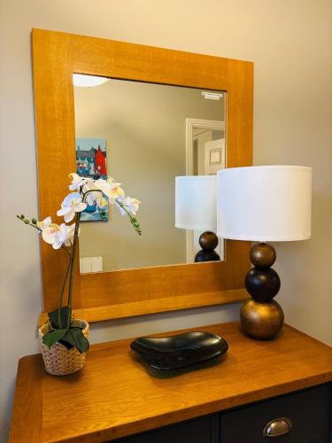a mirror on a dresser with a lamp and flowers at Boru Walk Townhouse -Stylish & Modern Holiday Home in Killaloe