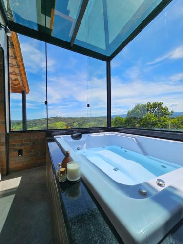 una vasca da bagno in una stanza con una grande finestra di Khaya Chalés - Chalés de Luxo na Serra para Casais com Hidro a Jaboticatubas