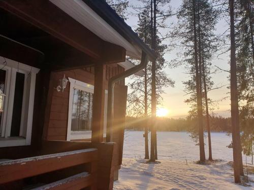 a house in the snow with the sun setting behind trees at Rantamökki 28 in Syöte