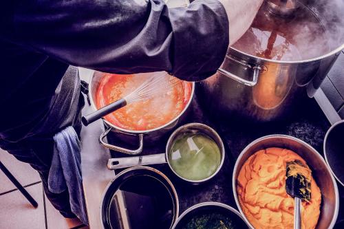 a person cooking food in pots on a stove at Hotell Mossbylund in Abbekås